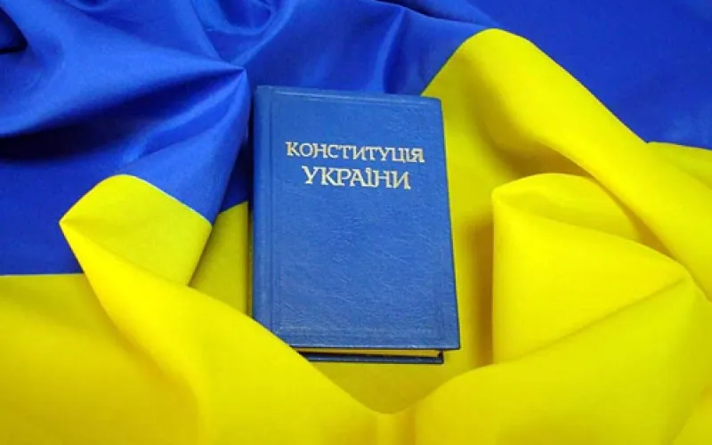 Книга «Конституція України» у синій обкладинці лежить на складеному синьо-жовтому прапорі — конституційні гарантії.