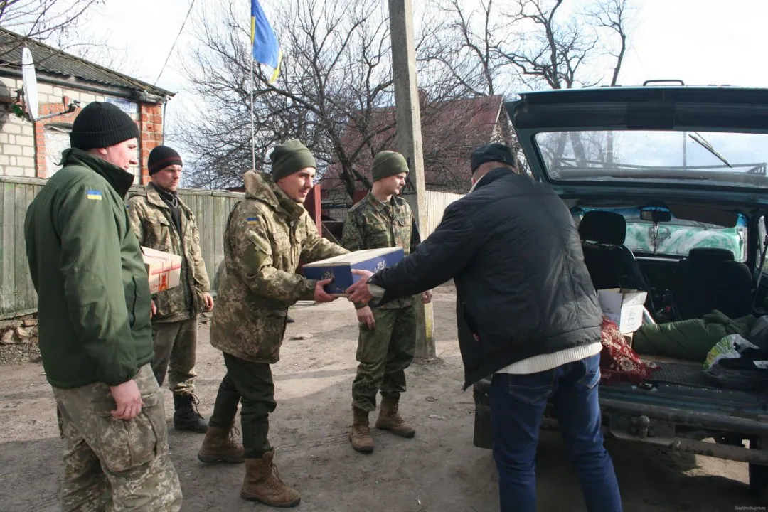 Військові передають картонні коробки гуманітарної допомоги цивільному біля відкритого багажника авто — волонтерська та гуманітарна діяльність.