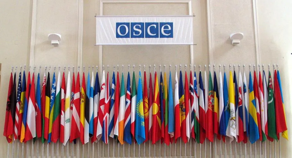 Настільні прапорці держав-учасниць у ряд під банером з логотипом OSCE (ОБСЄ) — регіональний механізм безпеки.
