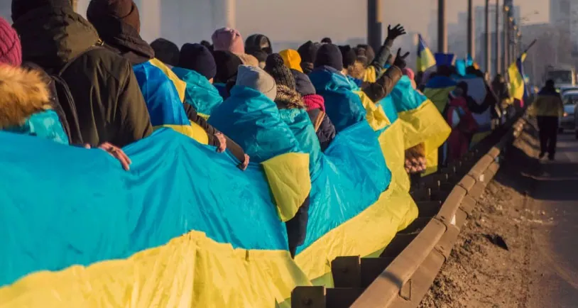 Колона людей на вулиці несе величезний прапор України вздовж дороги — патріотична акція, громадянська єдність.