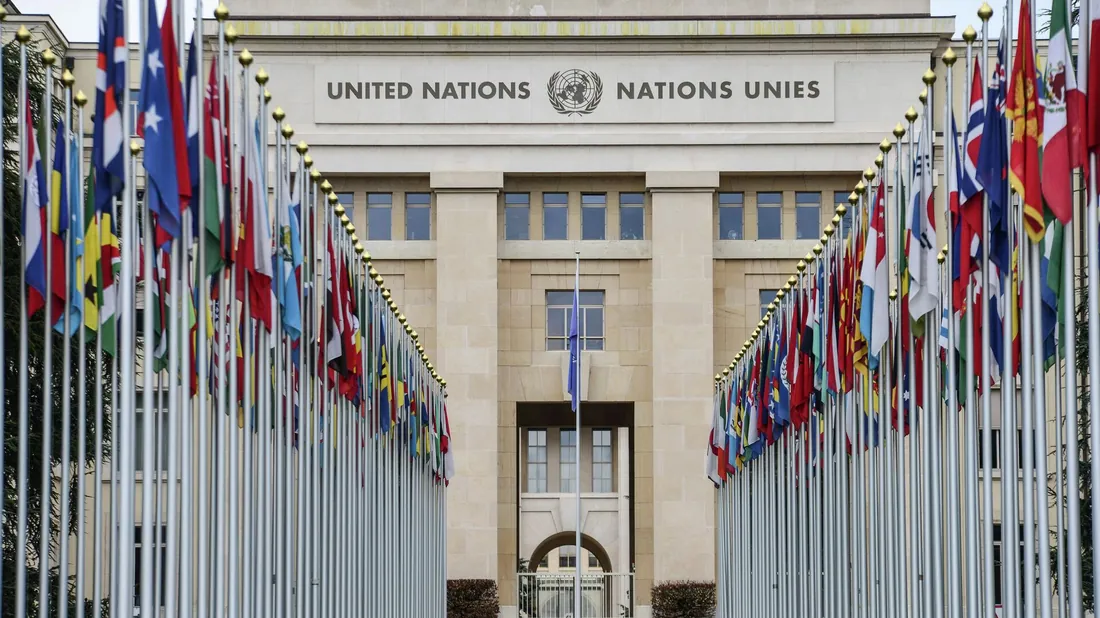 Палац націй у Женеві з написом UNITED NATIONS / NATIONS UNIES, перед входом дві алеї прапорів країн-членів — ООН як гарант міжнародної безпеки.
