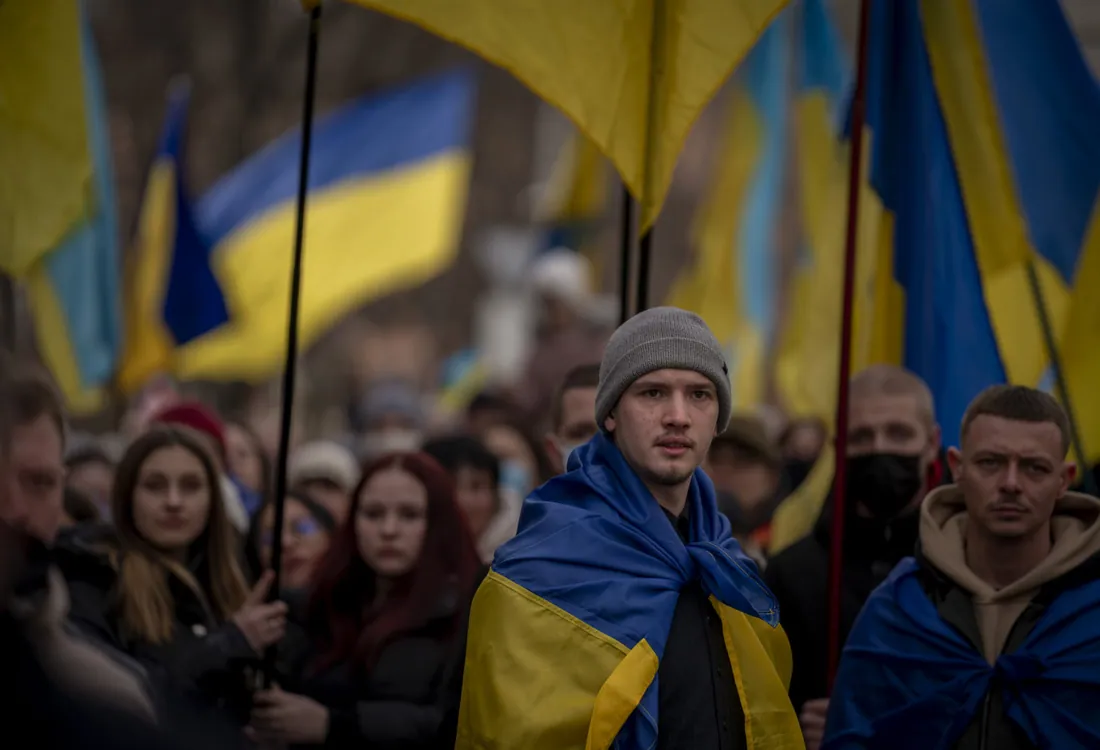 Мітинг: юнак у шапці загорнутий у прапор України, довкола натовп із синьо-жовтими прапорами — громадянська активність.