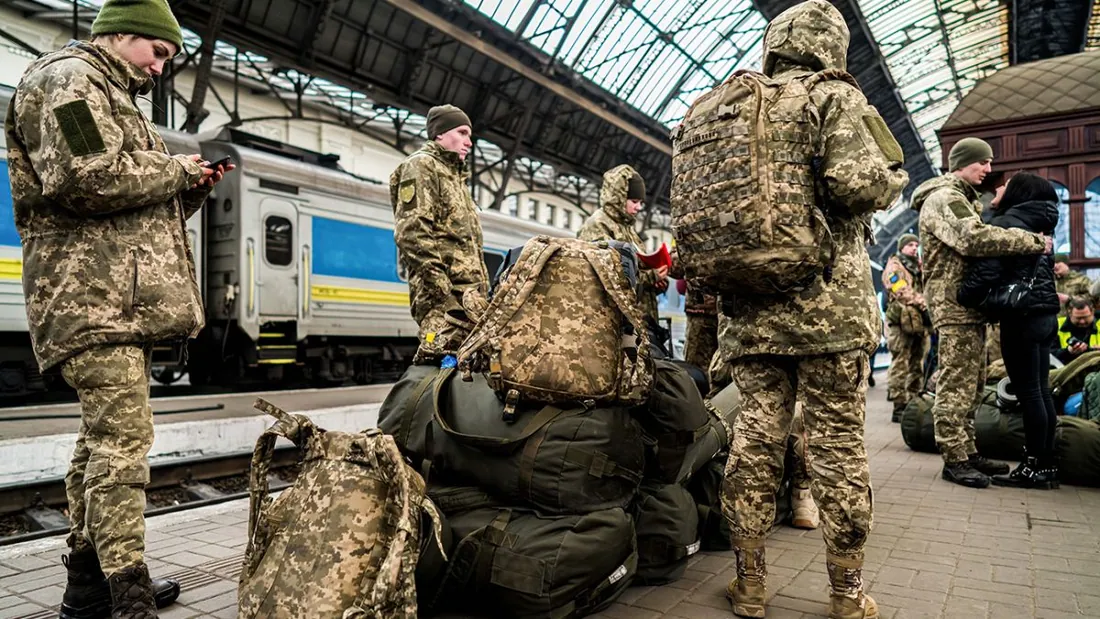 Військові з великими рюкзаками на пероні вокзалу біля вагона Укрзалізниці; один прощається з жінкою — відправка на…