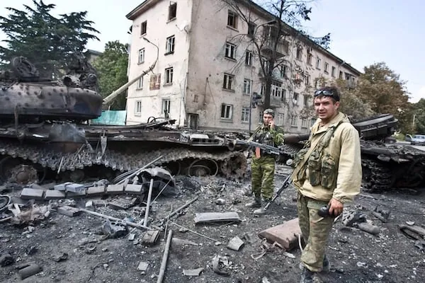 Підбитий танк із зірваною баштою біля зруйнованого багатоповерхового будинку, поруч стоять військові — війна в Абхазії…