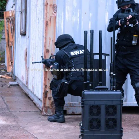 Бійці спецпідрозділу SWAT біля стіни будівлі; поруч на землі валізний блокувальник зв'язку з чотирма антенами й…