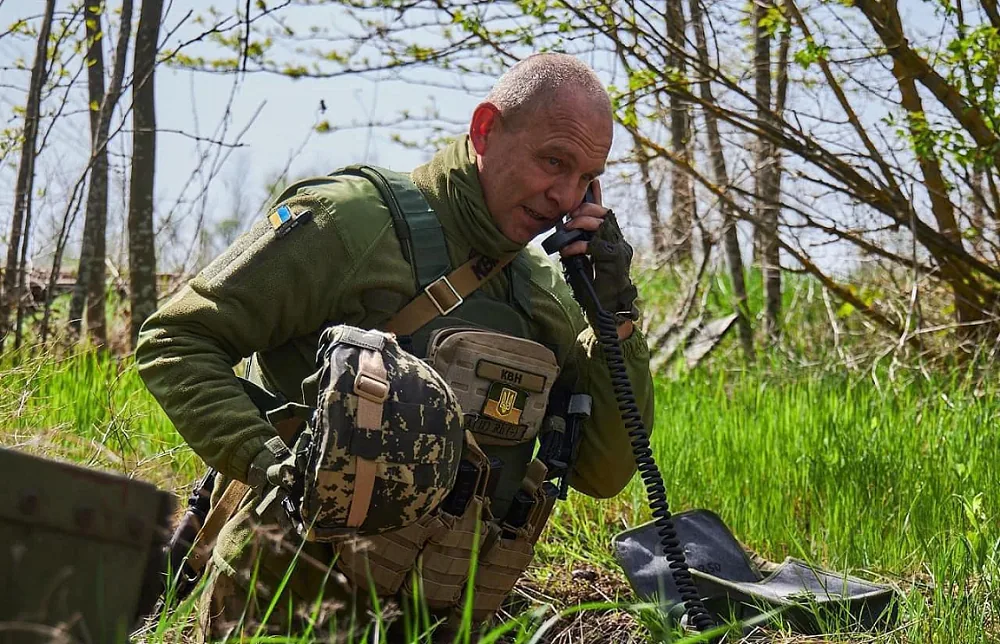 Військовий на колінах у зеленці говорить у трубку польової радіостанції, поруч ящики — прихованість зв'язку, робота в…