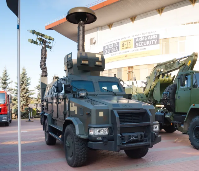 Український комплекс «Буковель» на виставці «Зброя та безпека»: бронеавтомобіль із двома щоглами — купольною й лог-періодичною антенами; на банері напис ARMS AND SECURITY, 8–11 October.