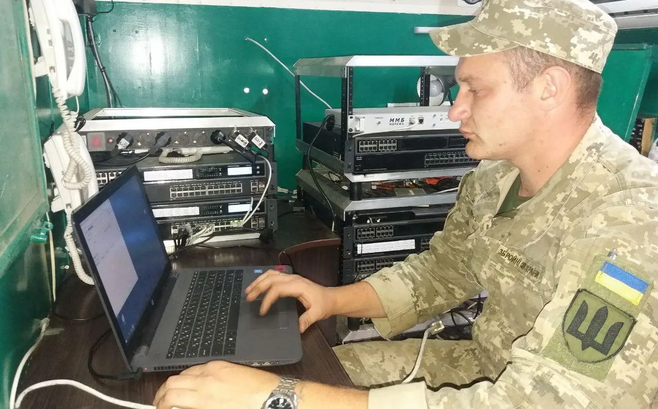 Військовий за ноутбуком у апаратній: поруч стійка з комутаторами, мультиплексорами й польовим телефоном…